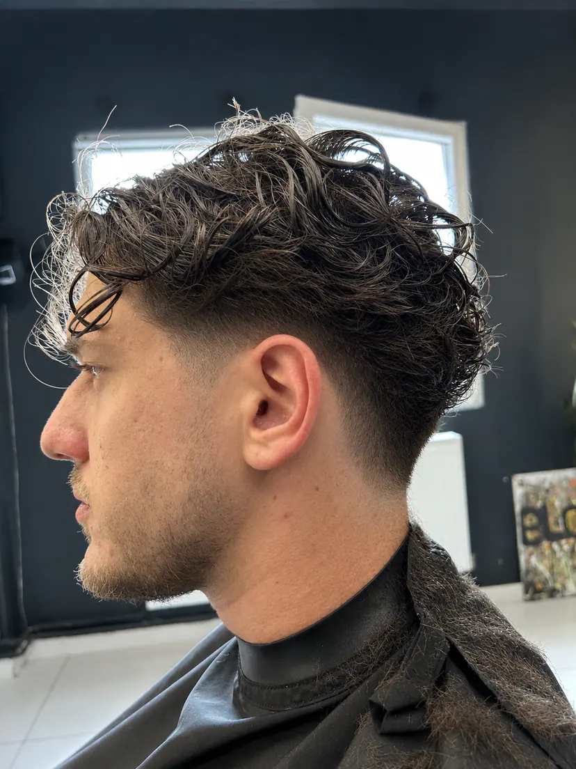 Tunsoare bărbătească cu bucle naturale deasupra și fade curat pe laterale, văzută din profil
